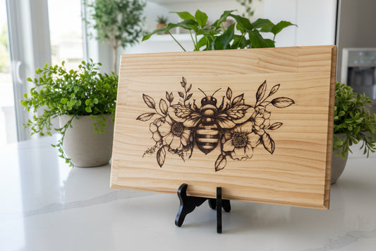 Wooden cutting board with floral and bee design on a white surface